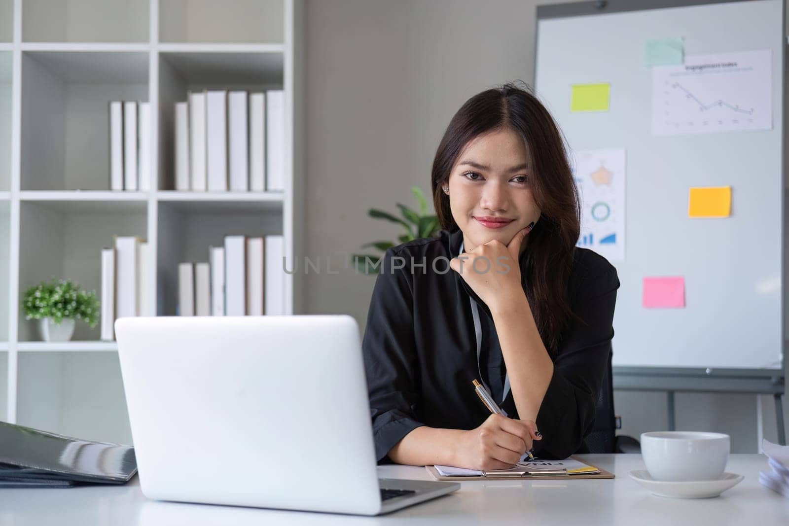 Beautiful smiling Asian businesswoman working using laptop and drinking coffee Asian businesswoman working with finance and calculator in her office.
