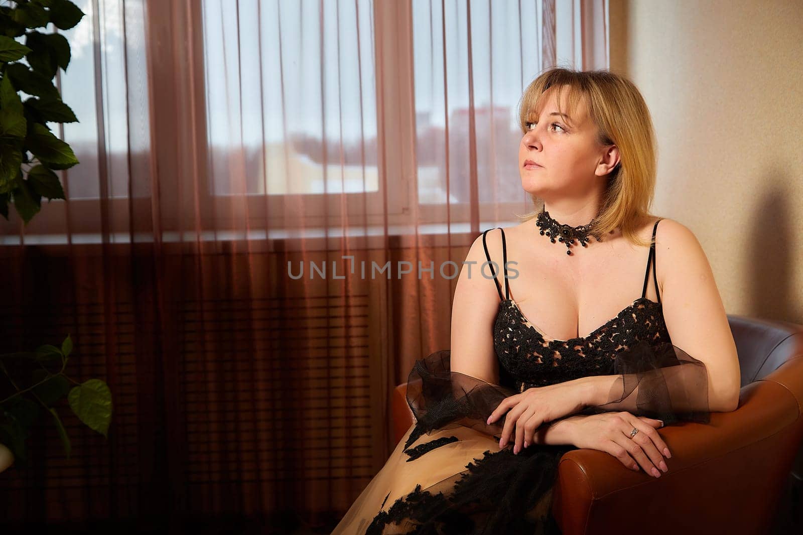 Portrait of beautiful elegant woman in in a royal dress indoors in nice room in evening time. Middle-aged adult lady in a romantic setting