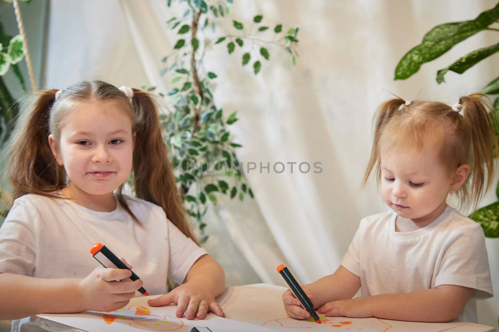 Cute little sisters are painting on table. Preschooler, 4 and 8 years child in living room. Small girl kids doing homework, home schooling concept