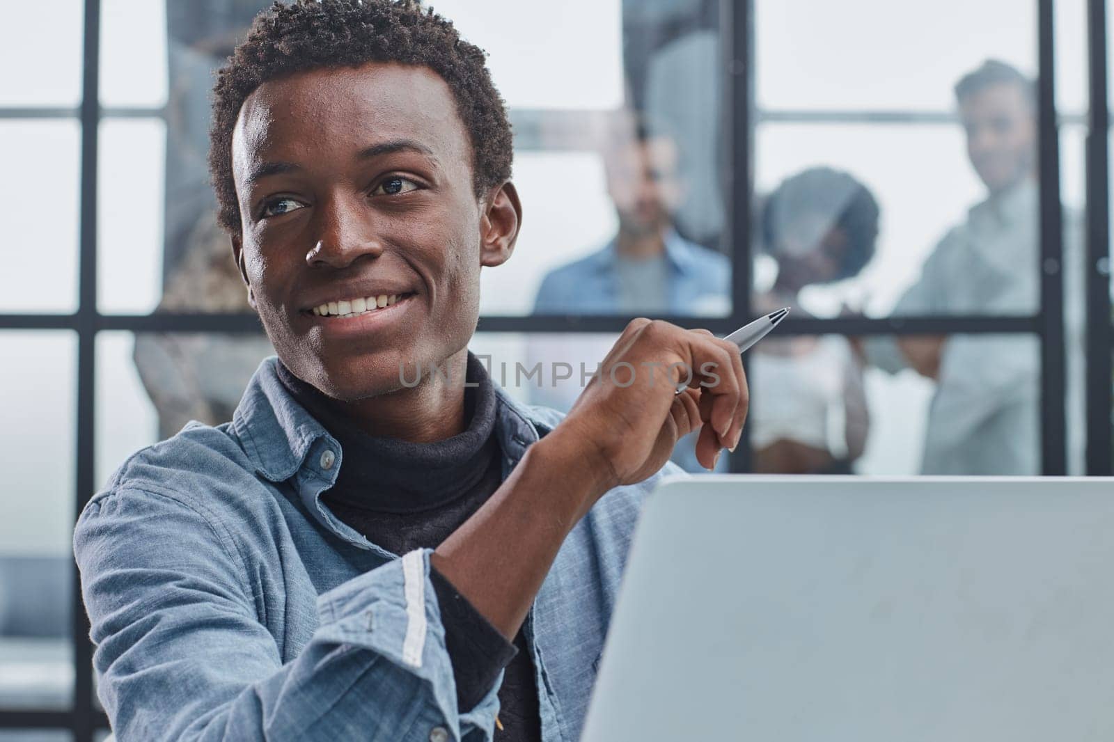 smiling leader business man with executives working on laptop in background.