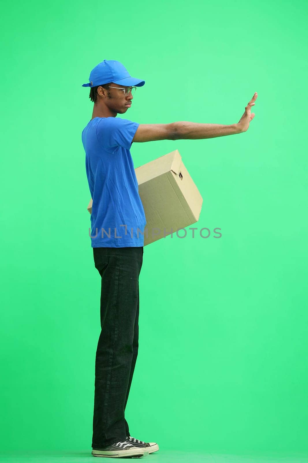 A male deliveryman, on a green background, in full height, with a box, shows a stop sign by Prosto