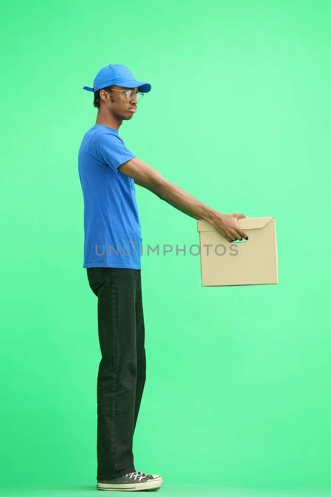 A male deliveryman, on a green background, in full height, gives a box by Prosto