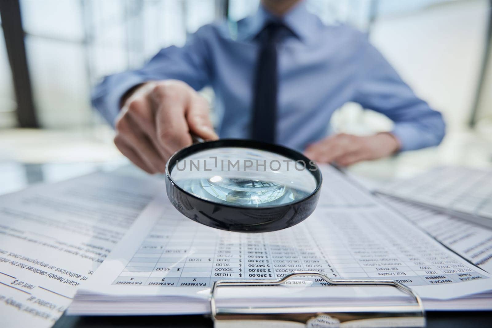 Businessman looking through a magnifying glass to documents by Prosto