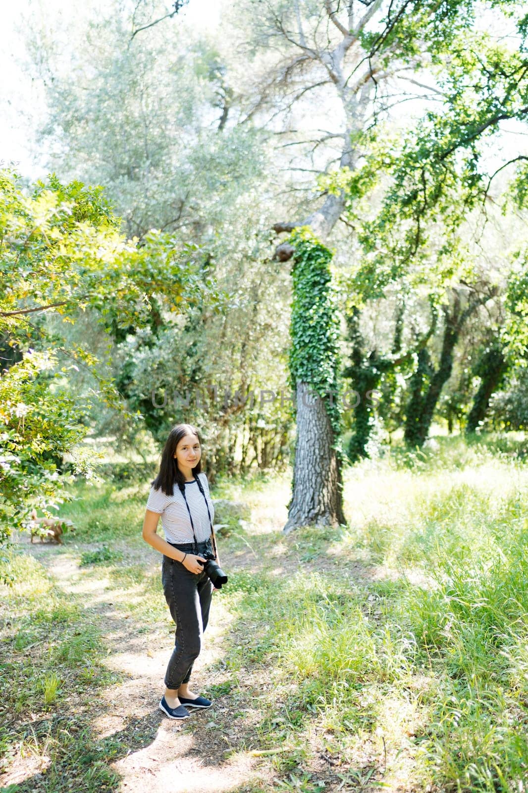 Photographer girl stands with a camera on a strap around her neck in the garden by Nadtochiy