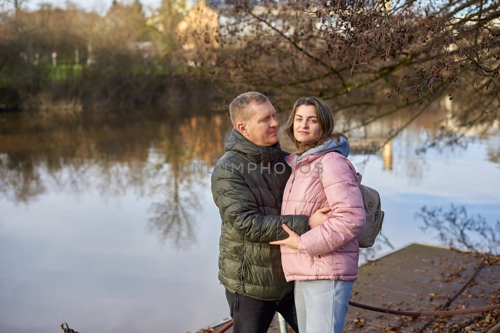 Loving couple on the shore of the pond in the park in autumn. A man and a woman. A couple, lovers on the shore of the lake on a walk. Autumn Romance by the Lake: Happy Couple's Lakeside Leisure. Seasons of Love: Couple's Tranquil Parkside Getaway by Andrii_Ko