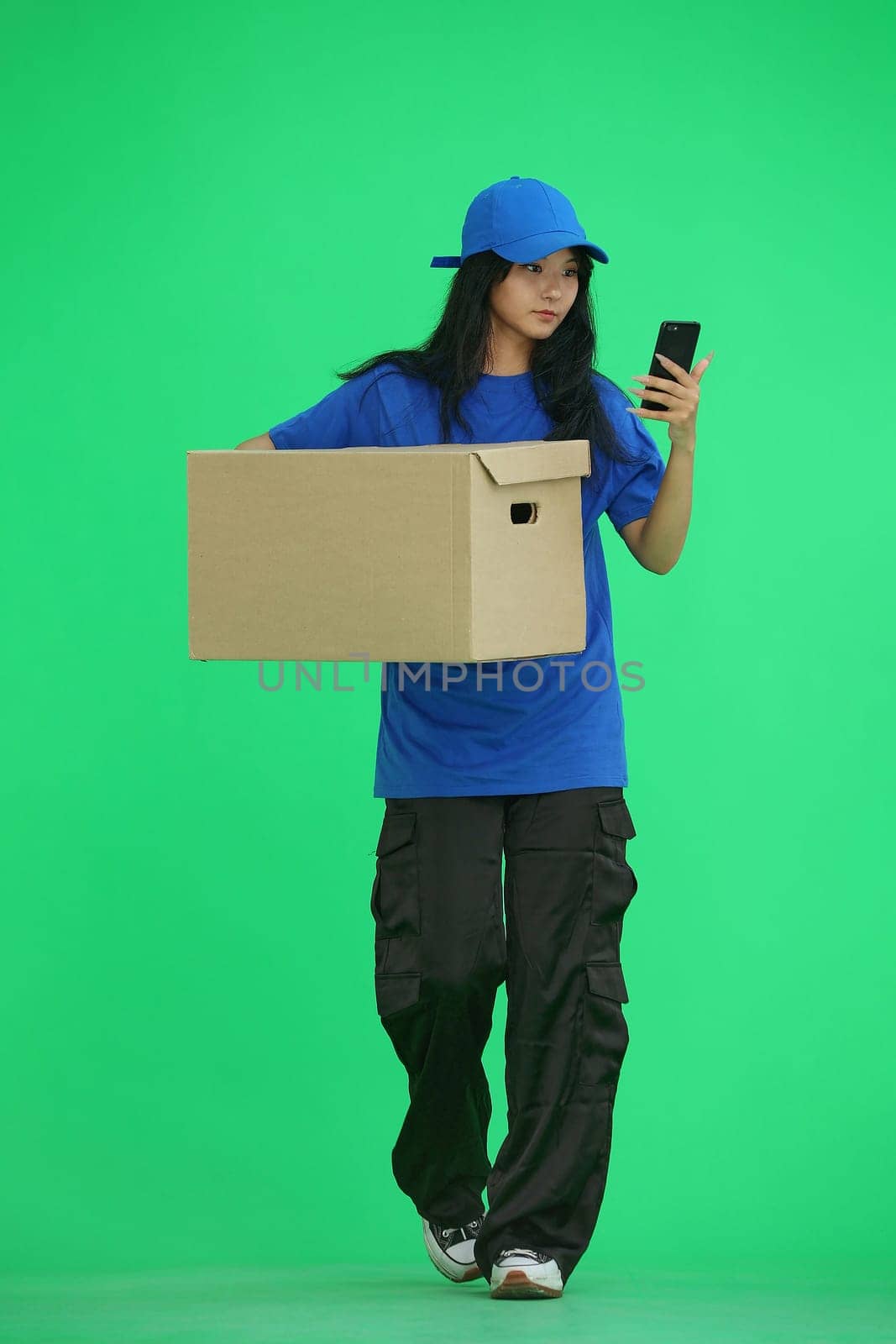 Delivery girl, on a green background, full-length, with a box and a phone.