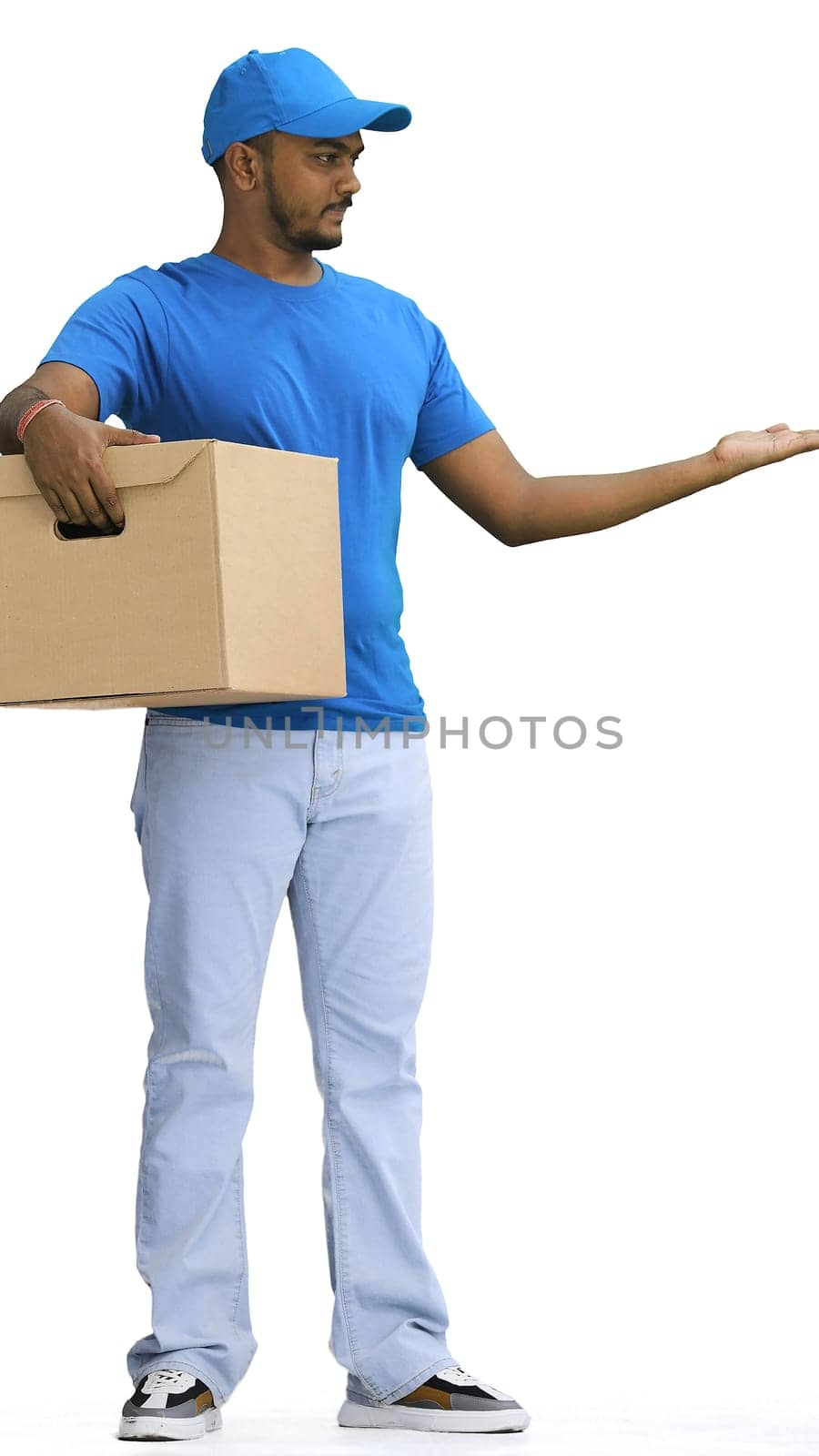 A male deliveryman with a box, on a white background, in full height, points to the side.