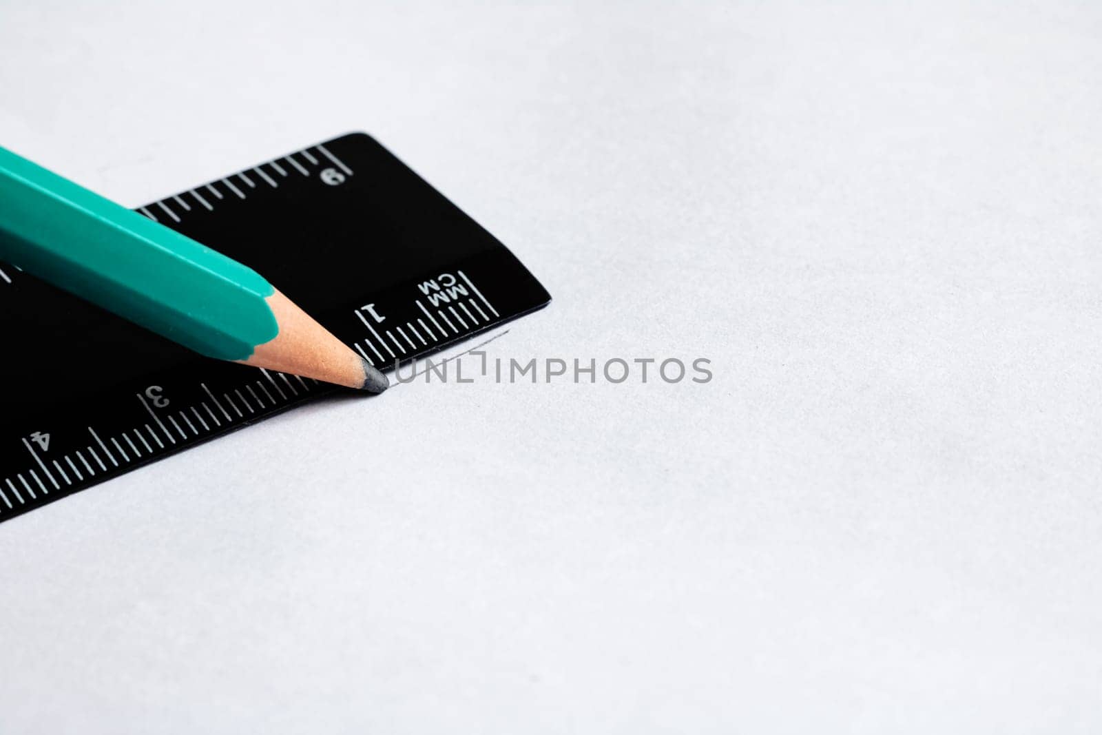 Green pencil and black ruler on a white background