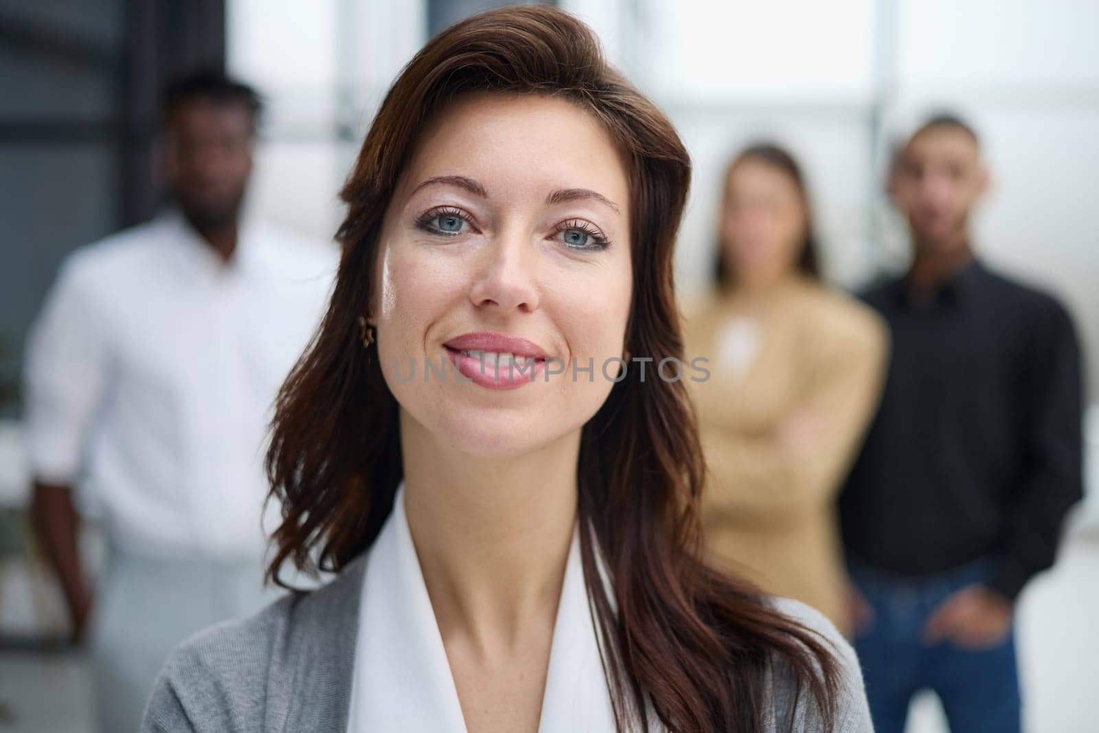 Portrait of a young woman standing in an office with colleagues in the background. by Prosto