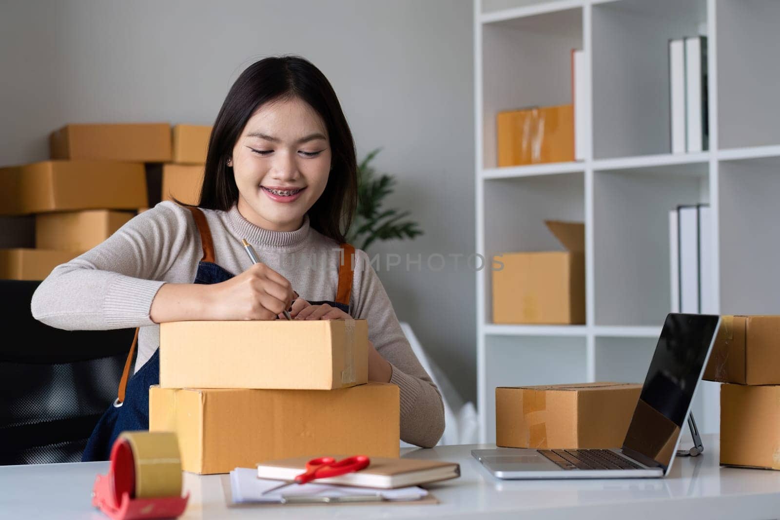 Startup SME small business entrepreneur SME or freelance Asian woman using a laptop with box, online marketing packaging box and delivery, SME concept. by wichayada