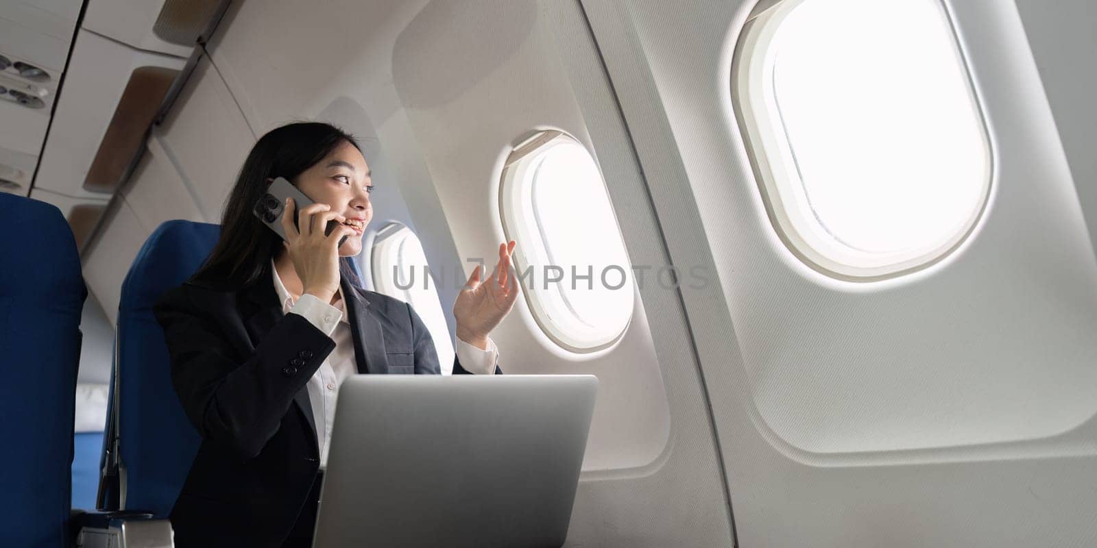 Successful young asian business woman sits in airplane cabin plane and working from anywhere. Flying at first class.