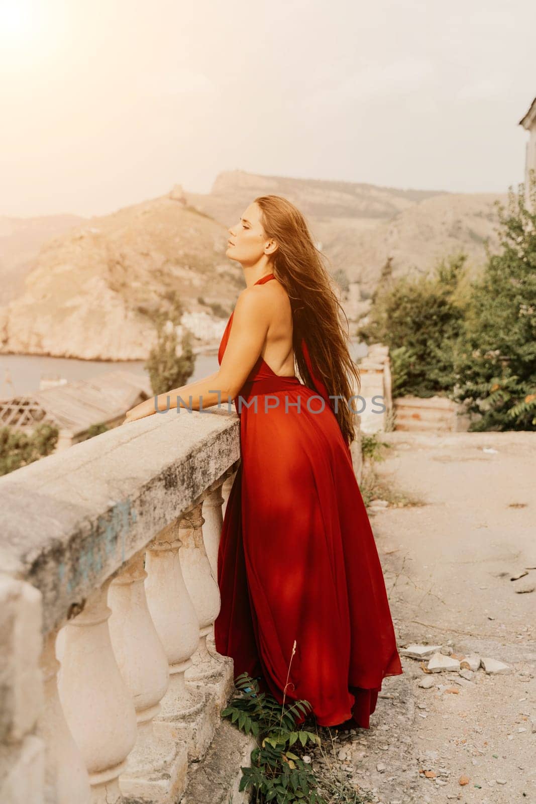Woman red dress. Summer lifestyle of a happy woman posing near a fence with balusters over the sea