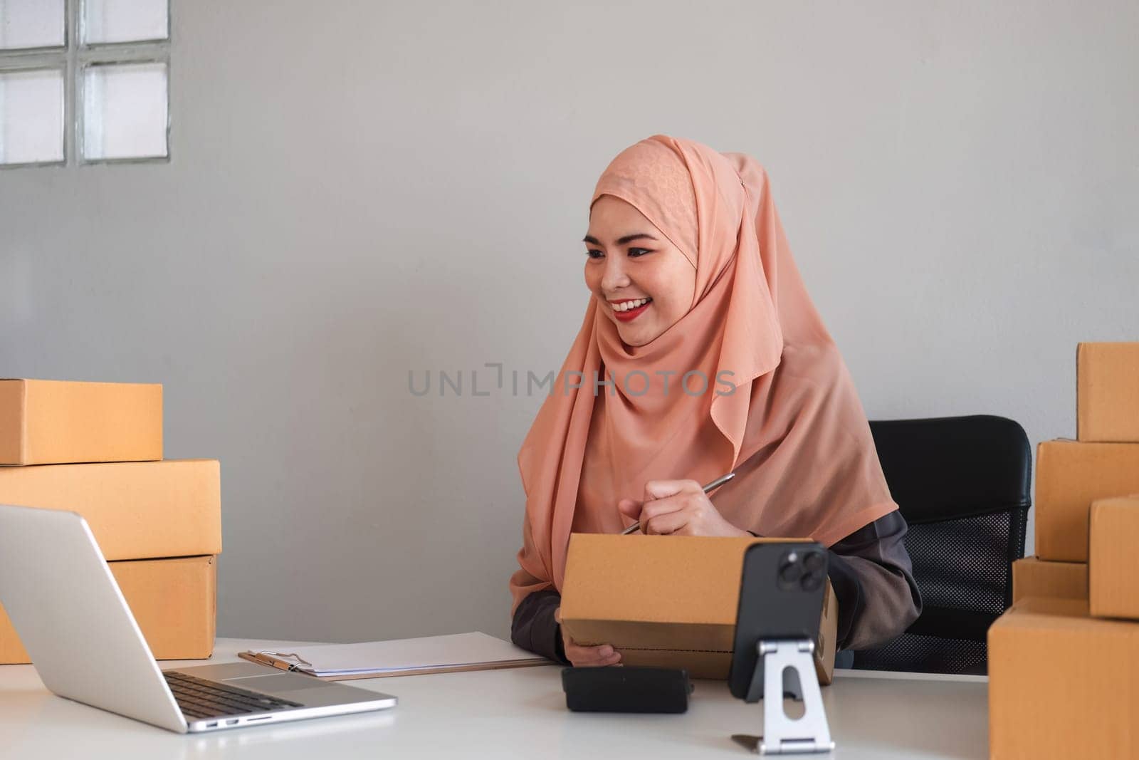 Asian Muslim businesswoman checks stock orders and saves them on her home office laptop. small business owner Shipping in online markets The concept of freedom in life by wichayada