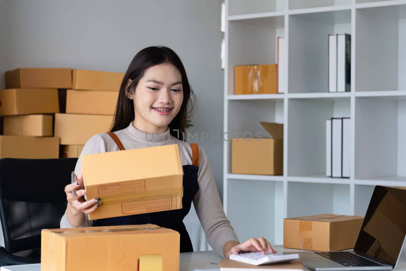 Startup SME small business entrepreneur SME or freelance Asian woman using a laptop with box, online marketing packaging box and delivery, SME concept..
