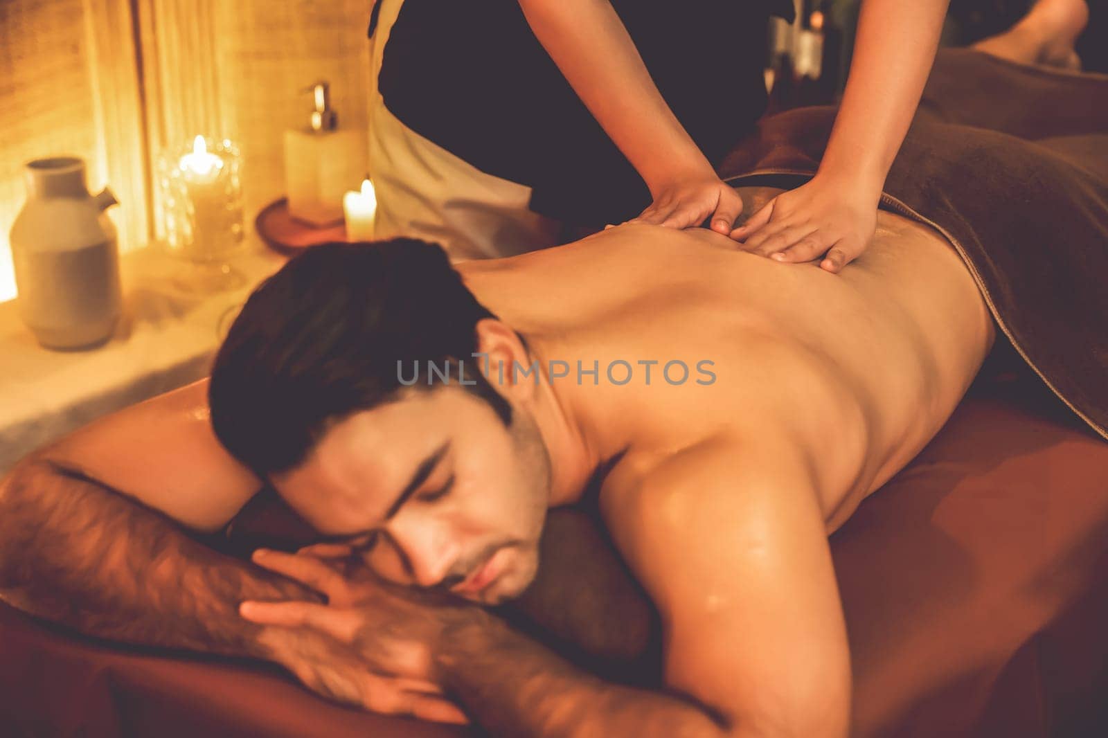 Caucasian man customer enjoying relaxing anti-stress spa massage and pampering with beauty skin recreation leisure in warm candle lighting ambient salon spa at luxury resort or hotel. Quiescent