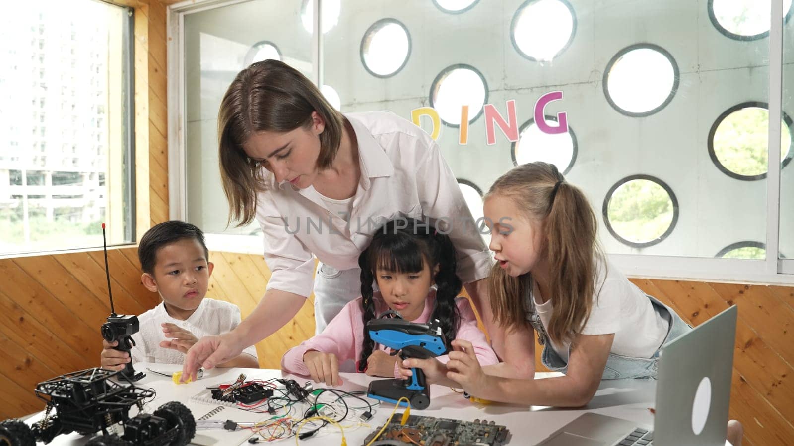 Teacher looking at children while diverse student looking at screen. Children excited in presentation while drawing or writing art books at table with toys and color pencil placed on table. Erudition.