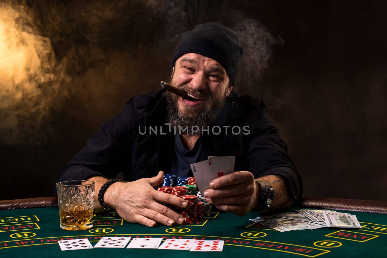 Bearded man with cigar and glass sitting at poker table in a casino. Gambling, playing cards and roulette. by nazarovsergey