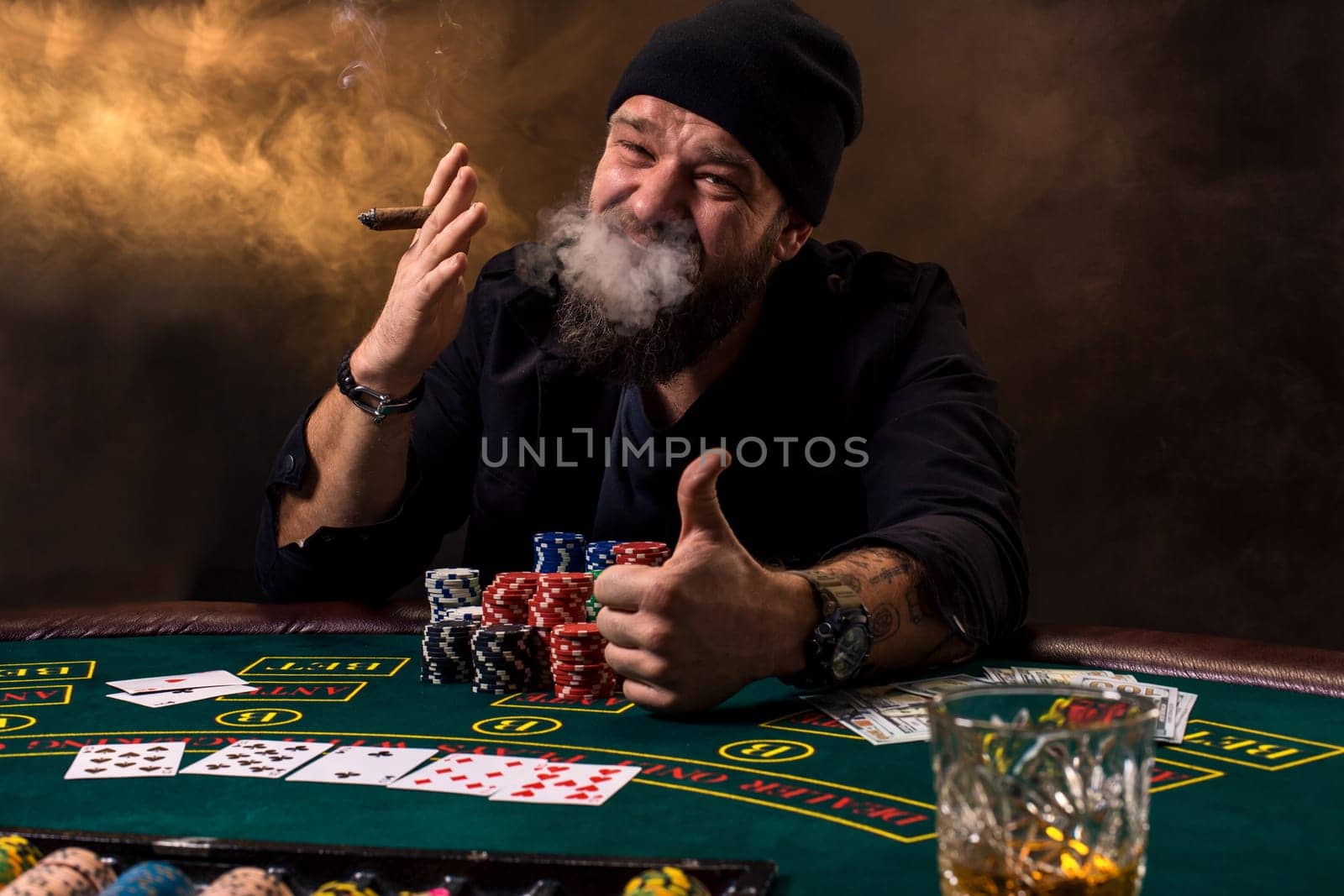 Bearded man with cigar and glass sitting at poker table in a casino. Gambling, playing cards and roulette. by nazarovsergey