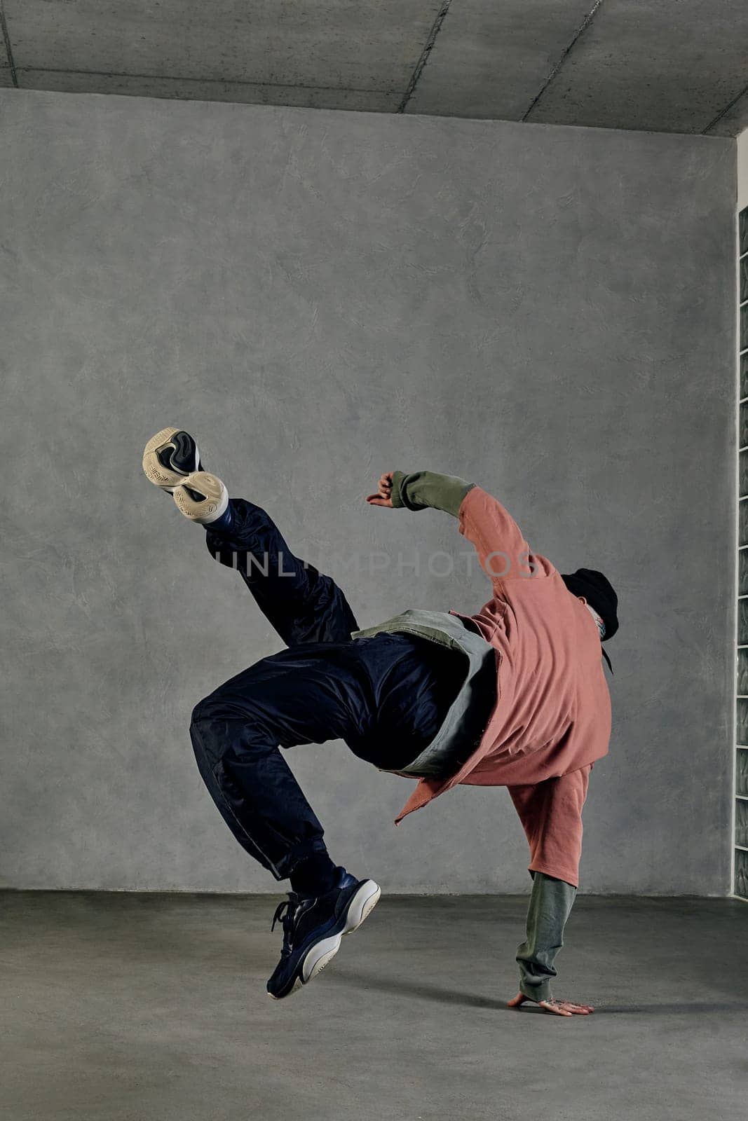 Stately male with tattooed body and face, earrings, beard. Dressed in colorful jumper, black pants and sneakers. Dancing on gray background. Dancehall, hip-hop. Full length, copy space