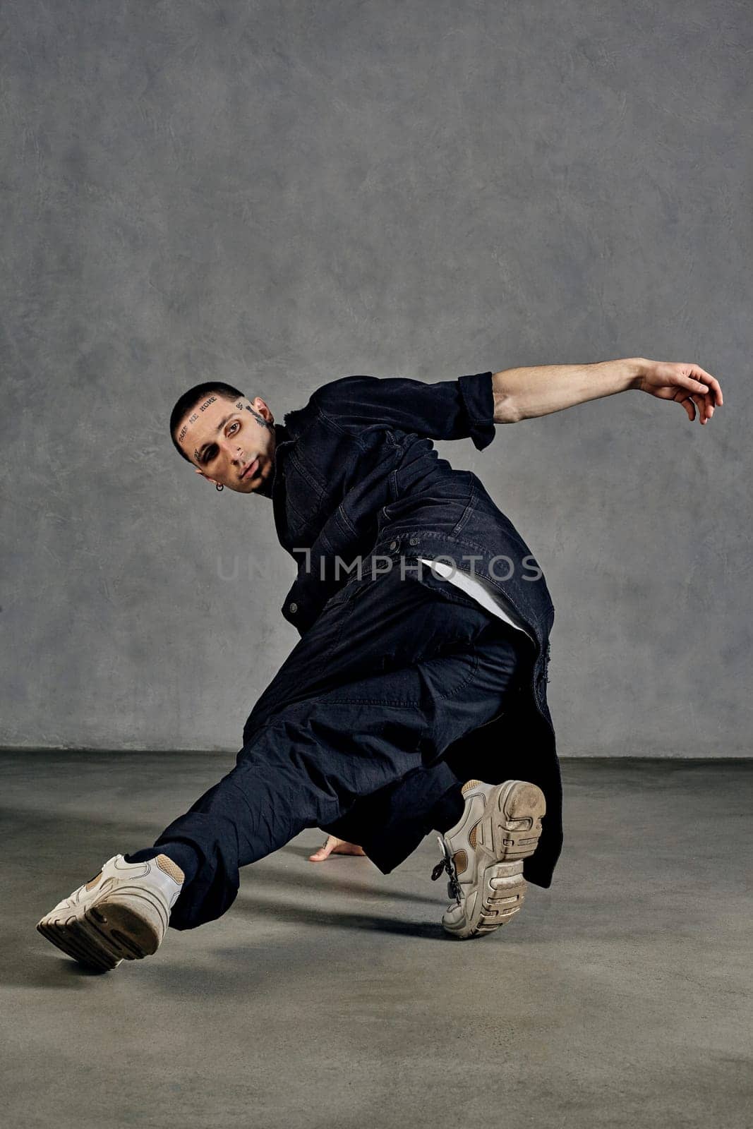 Flexible male, tattooed body, beard. Dressed in white t-shirt and sneakers, black denim shirt, pants. Dancing on gray background. Dancehall, hip-hop by nazarovsergey