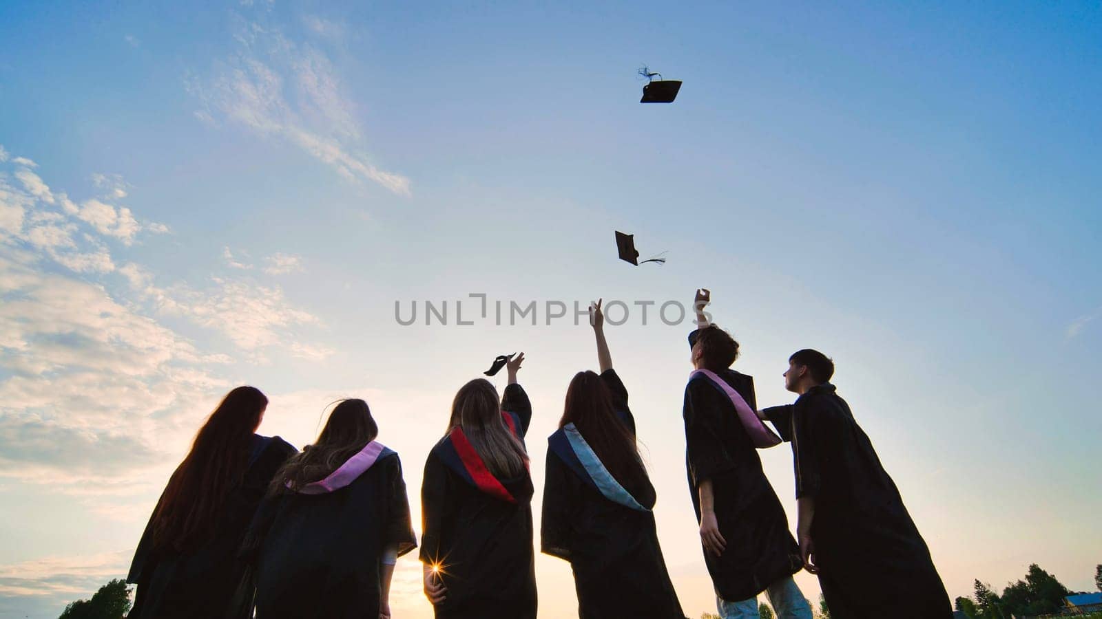 Student graduates toss their caps at sunset