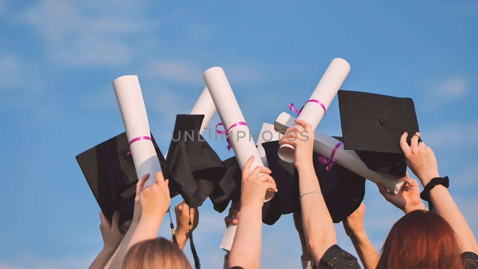 College graduates raise their caps and diplomas upward. by DovidPro