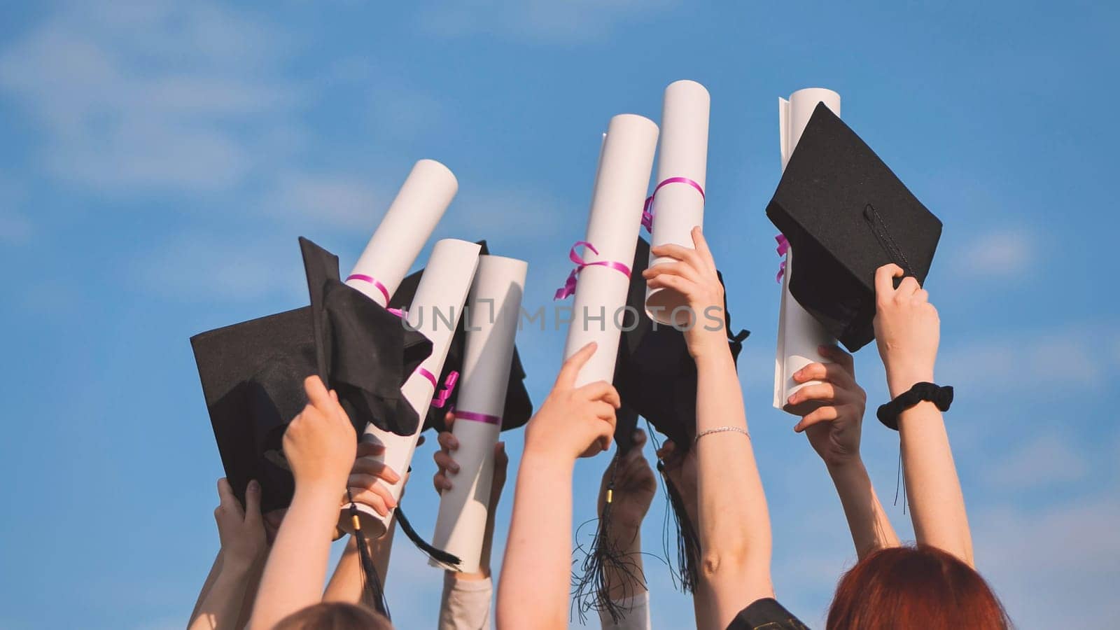 College graduates raise their hands with caps and diplomas to the sky. by DovidPro