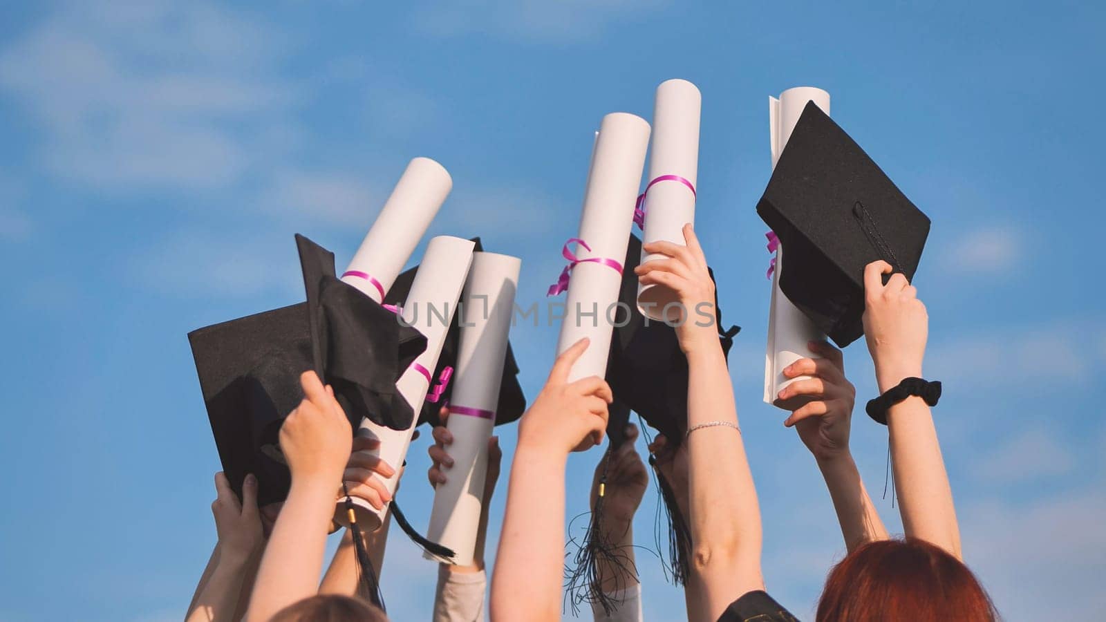 College graduates raise their hands with caps and diplomas to the sky