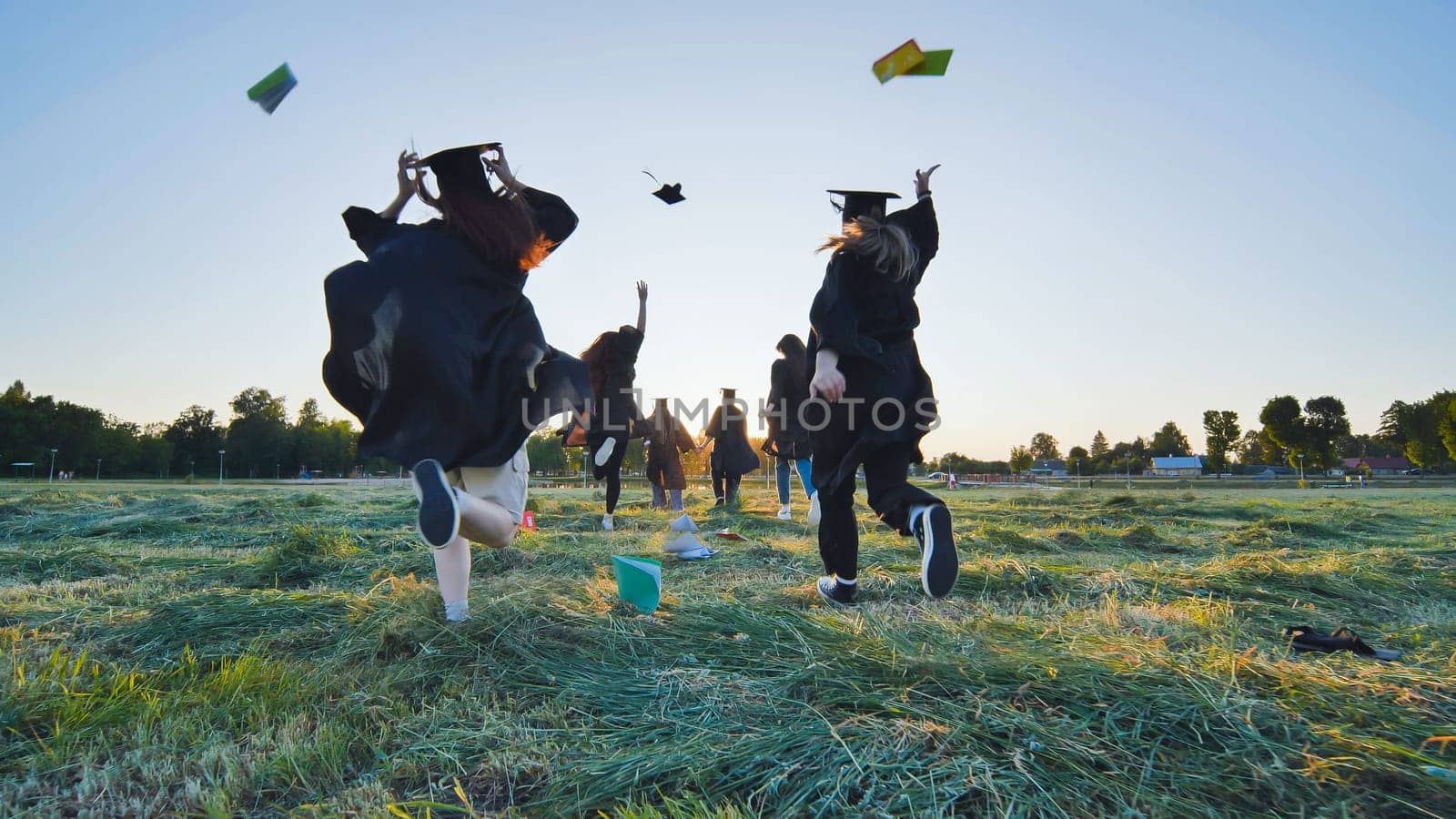 Cheerful graduates students run throwing notebooks after school at sunset