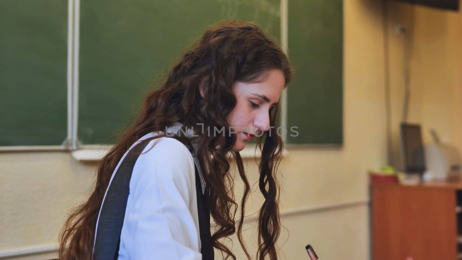 Schoolgirl as a teacher sits at a desk and writes something
