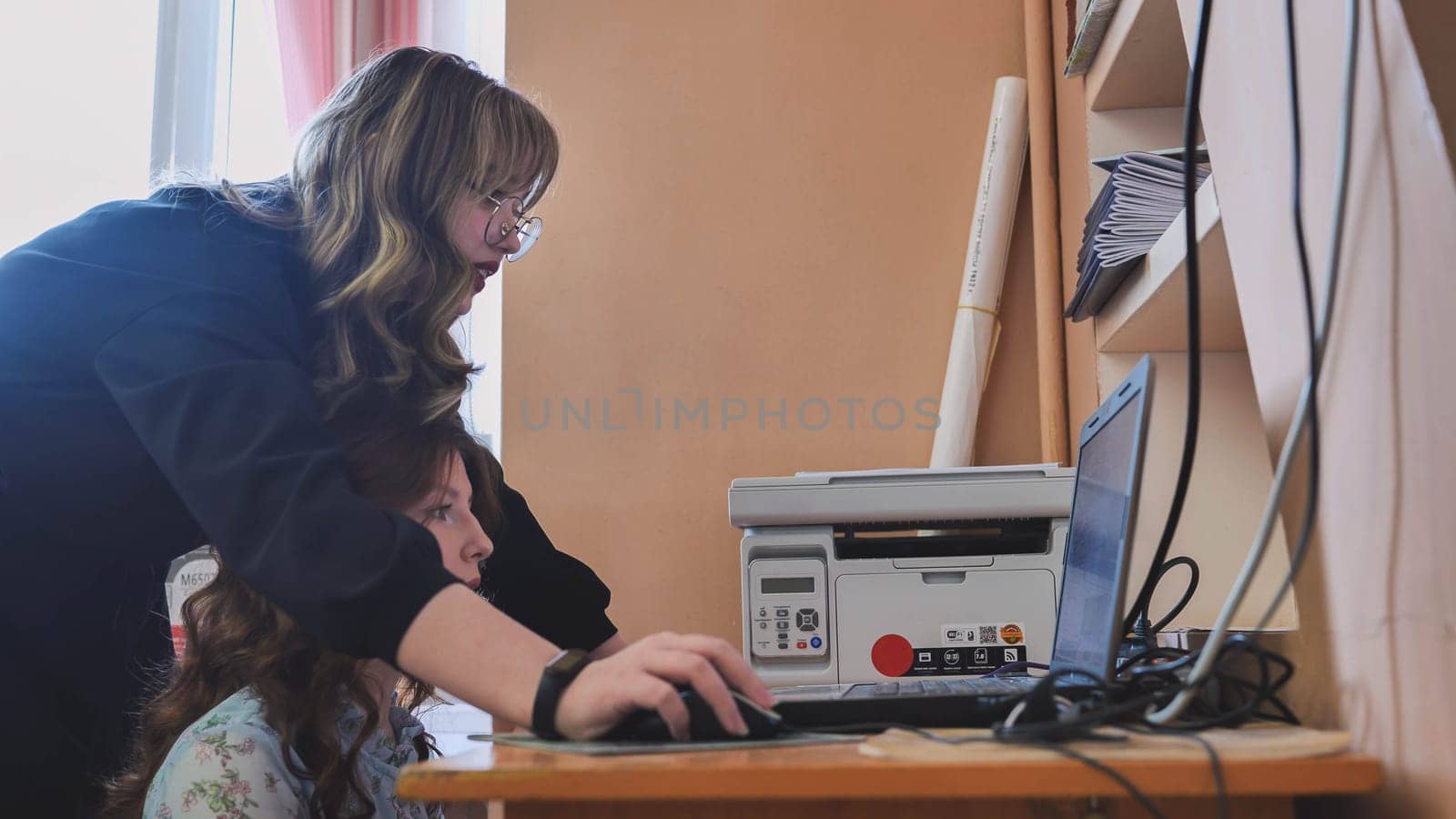Two female students are working at a computer in a classroom at school. by DovidPro