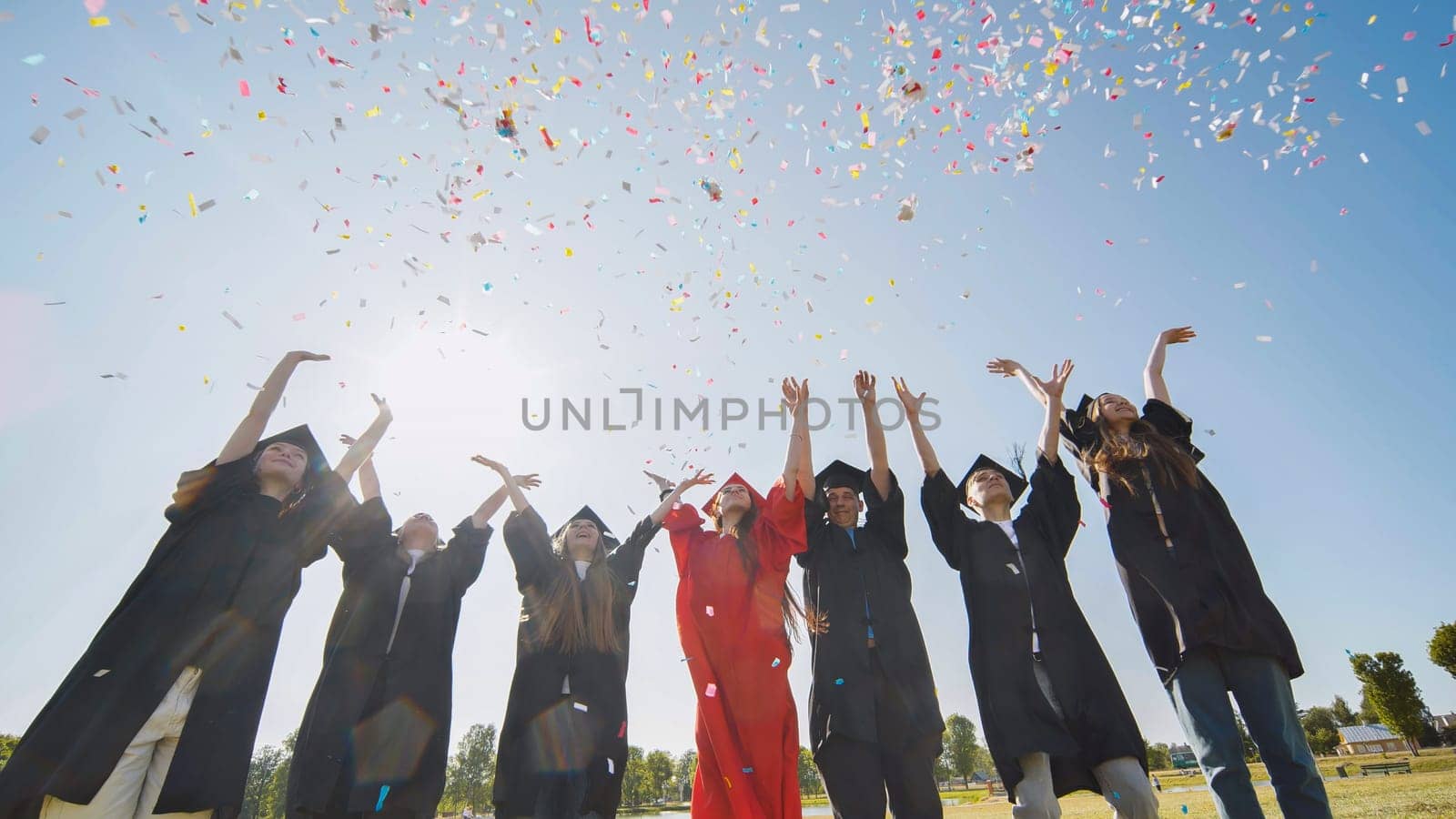Happy college graduates throw colorful confetti against the rays of sunshine