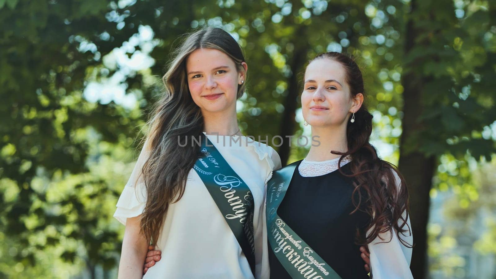 Portrait of two Russian schoolgirls graduating from high school with a ribbon and the name - Graduate 2023 on it. by DovidPro