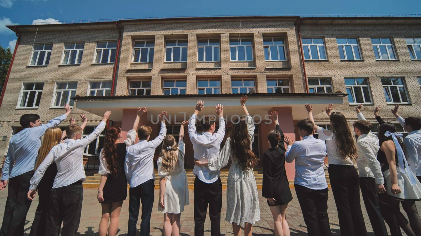Berezovka, Belarus - May 31, 2023: Graduates say goodbye to the school and wave goodbye. by DovidPro