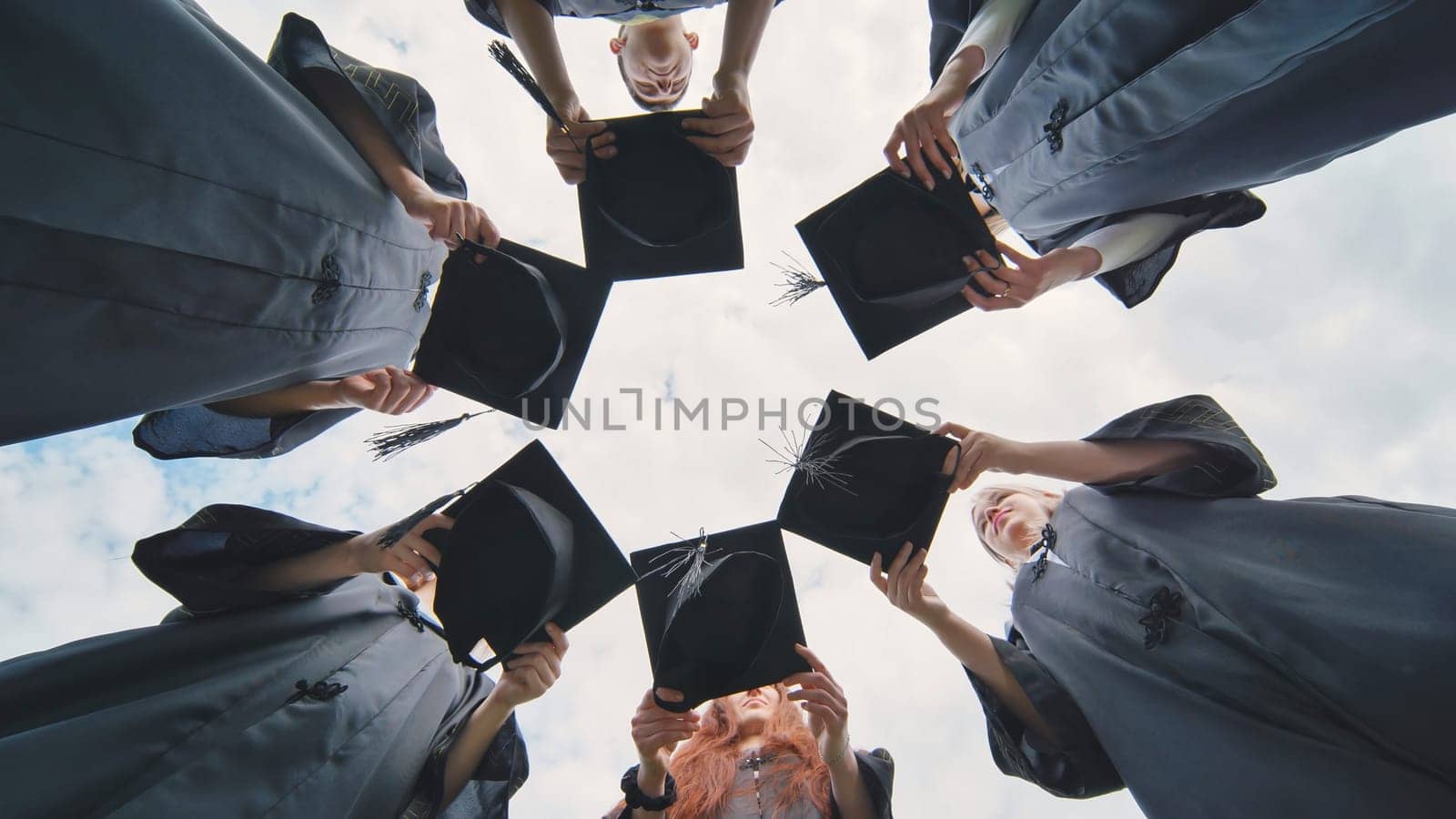 Graduates in black robes join their caps in a circle