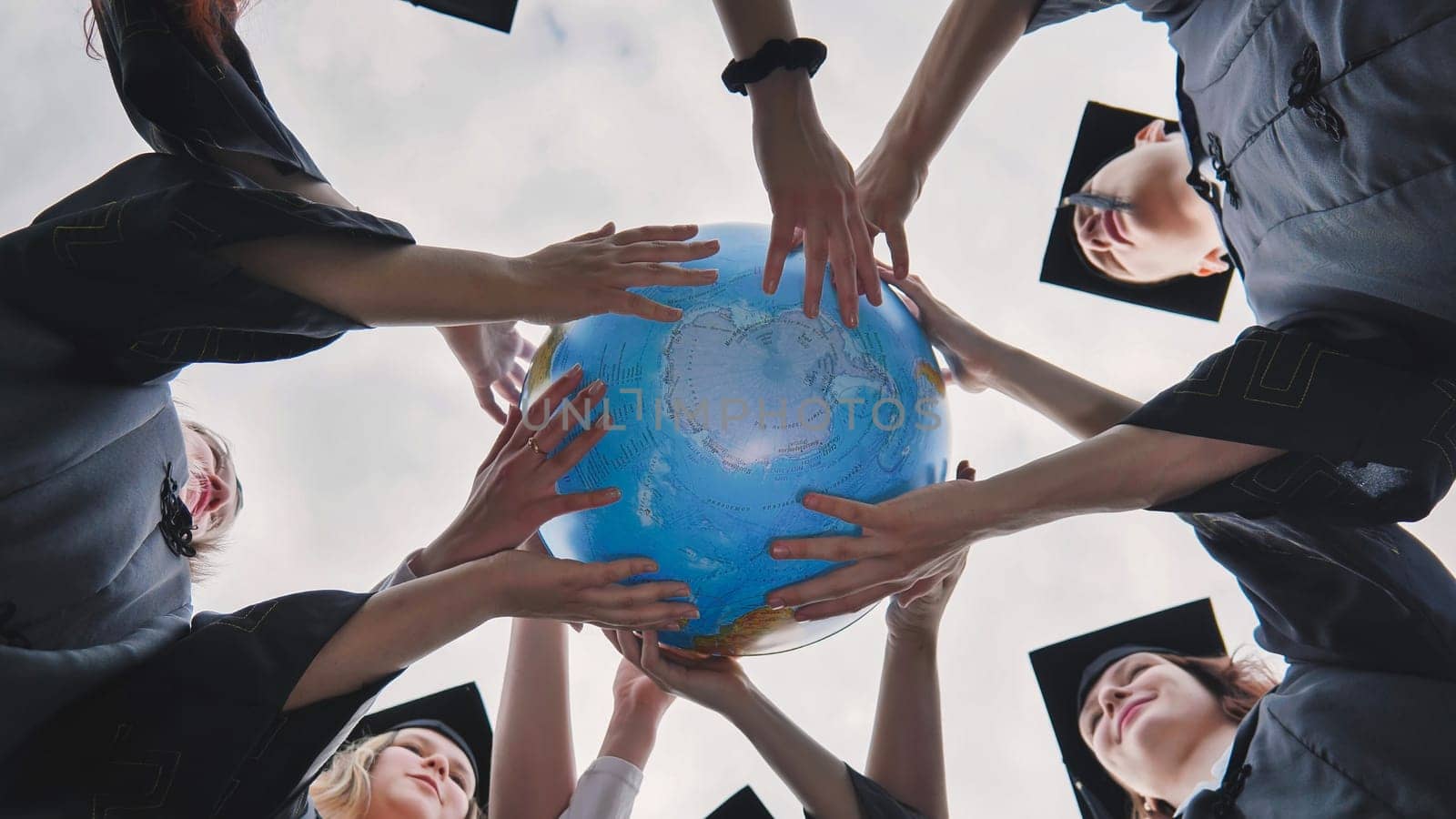 The concept of a world without war. College graduates holding a geographical globe of the world. by DovidPro