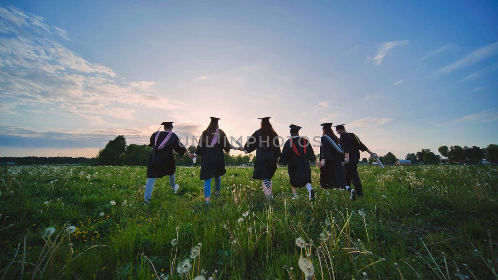 Six graduates in robes walk against the backdrop of the sunset. by DovidPro