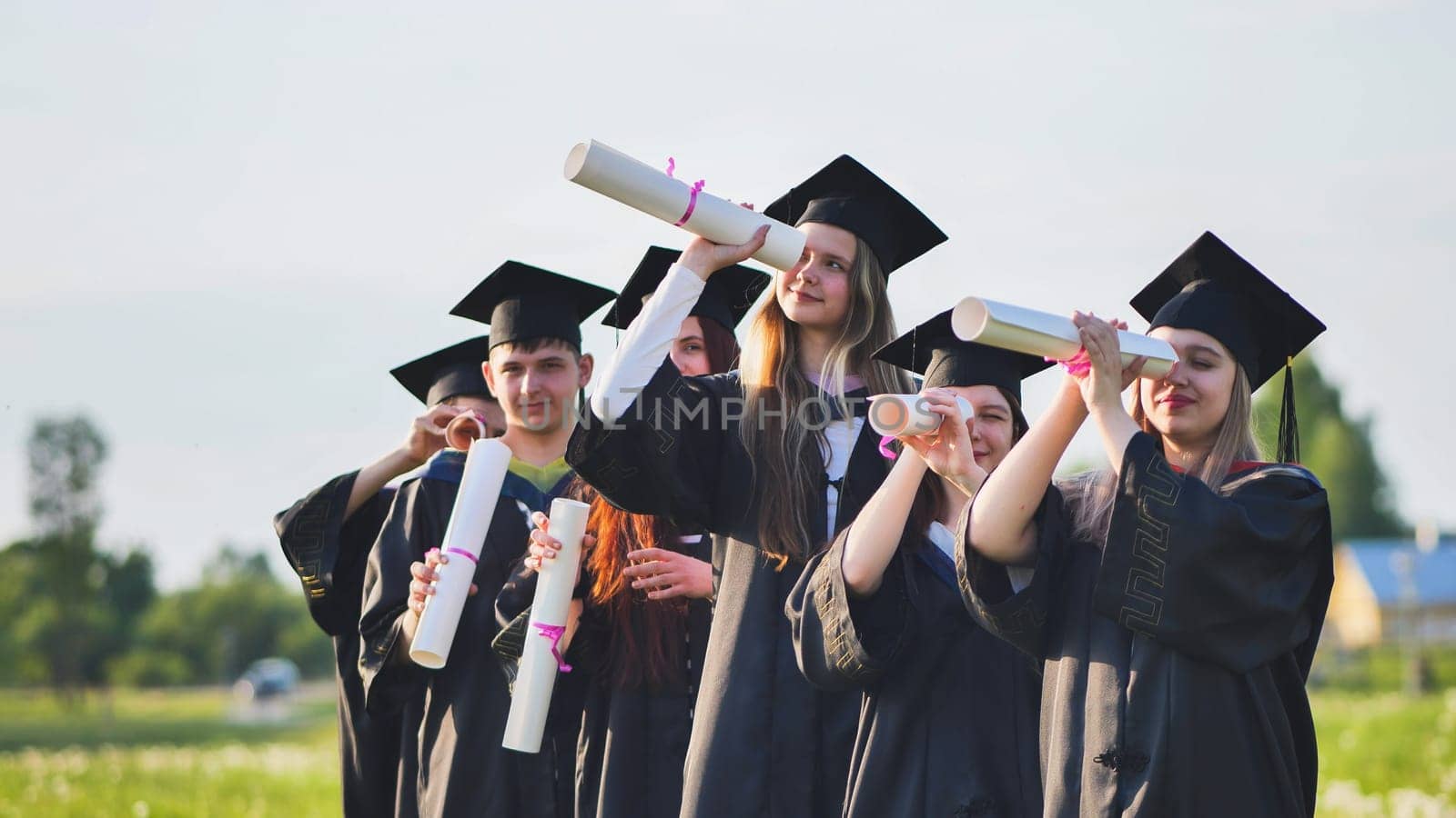 Cheerful graduates on a sunny day look through diplomas like a telescope