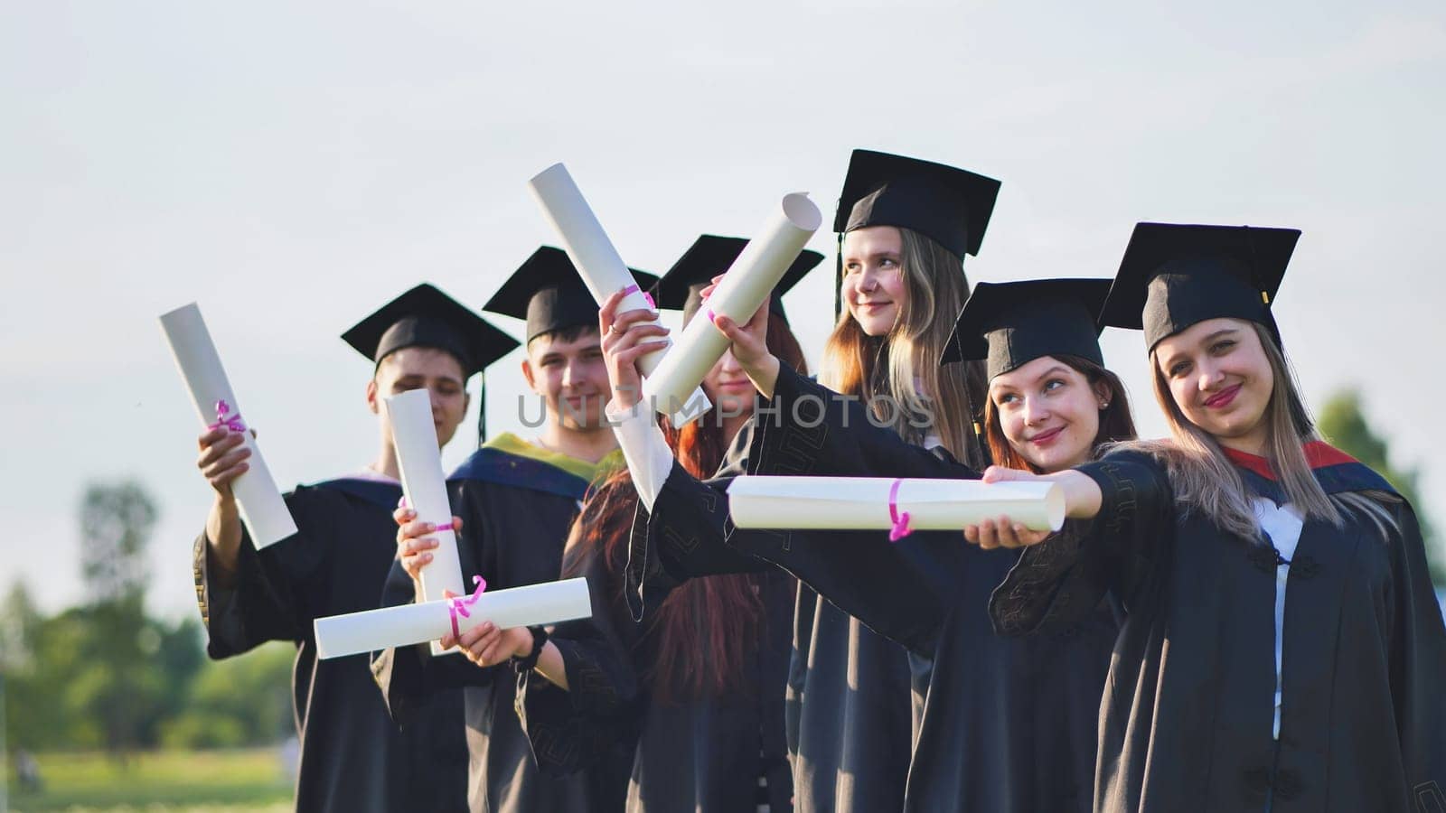 Cheerful graduates pose with raised diplomas on a sunny day. by DovidPro