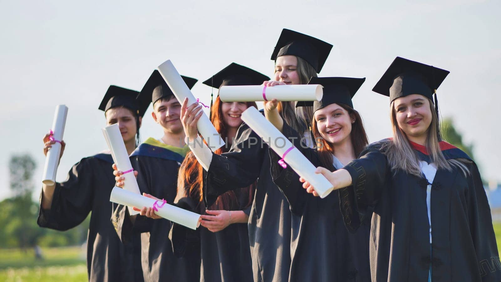 Cheerful graduates pose with raised diplomas on a sunny day