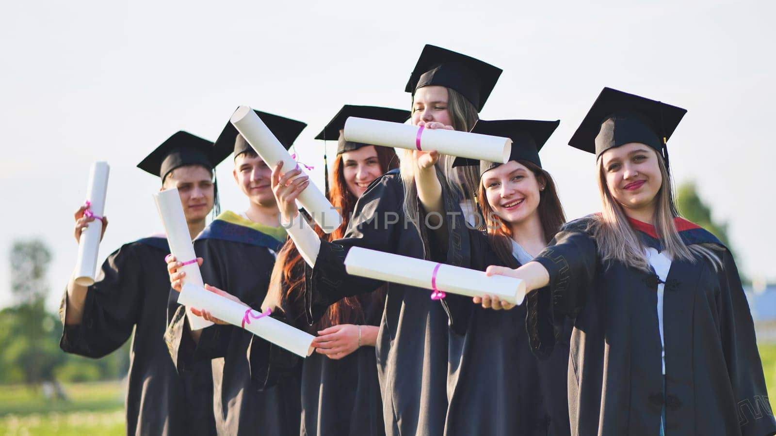 Cheerful graduates pose with raised diplomas on a sunny day