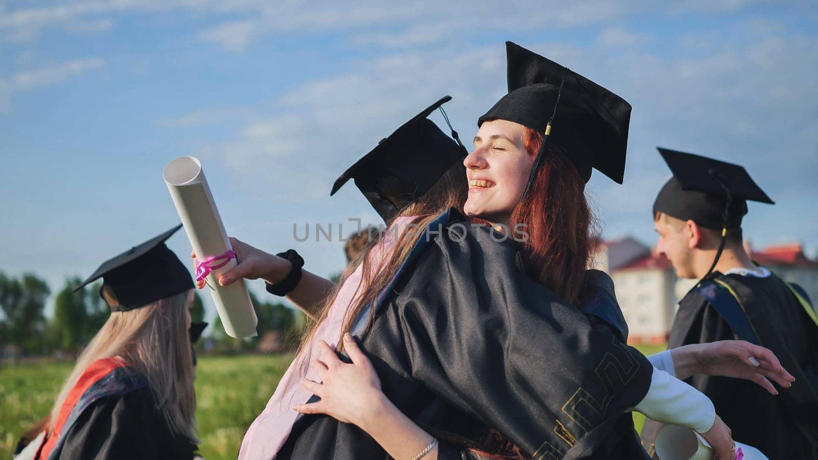 Two college graduates girls hugging on a sunny day. by DovidPro