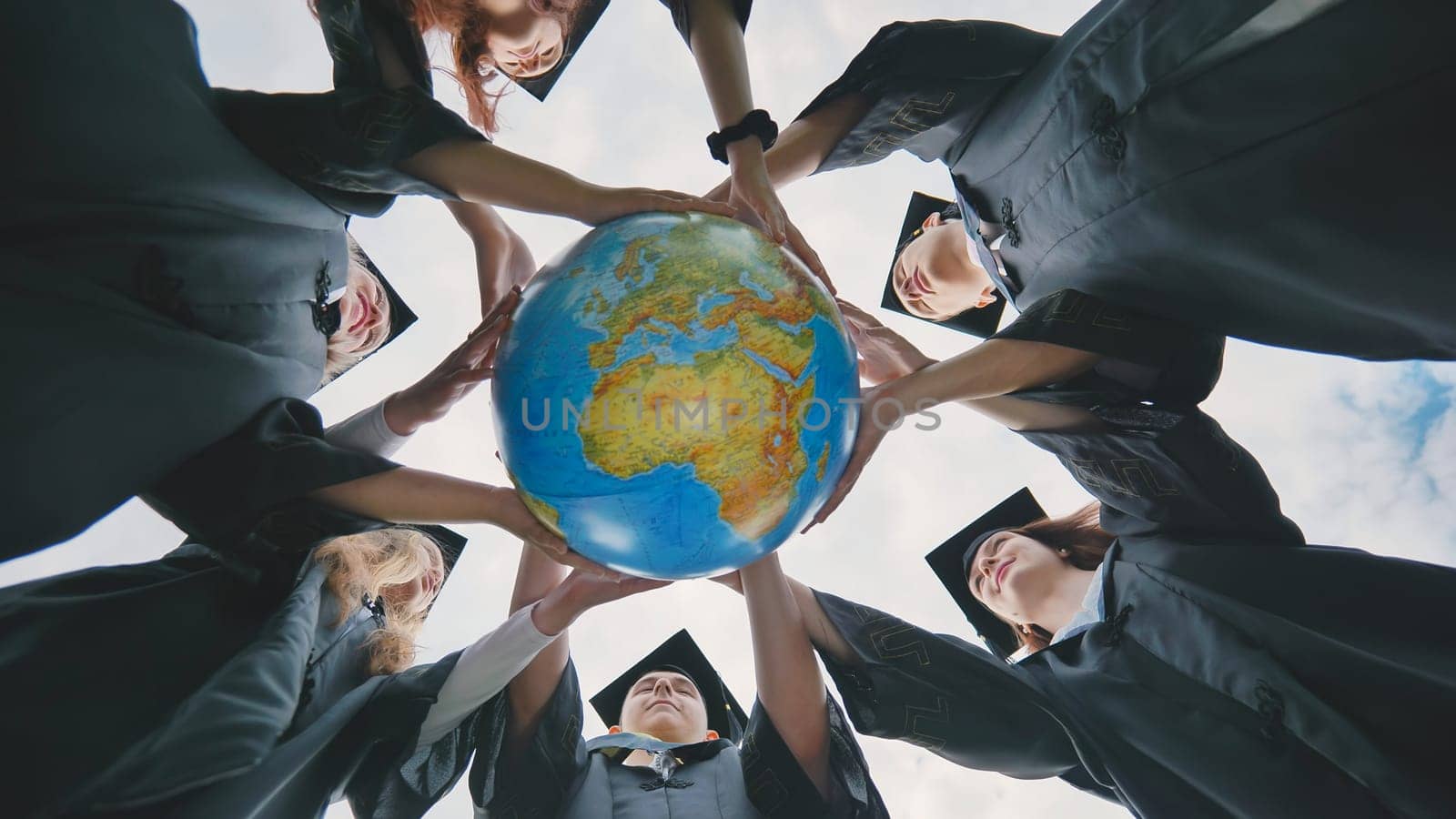 The concept of a world without war. College graduates holding a geographical globe of the world. by DovidPro