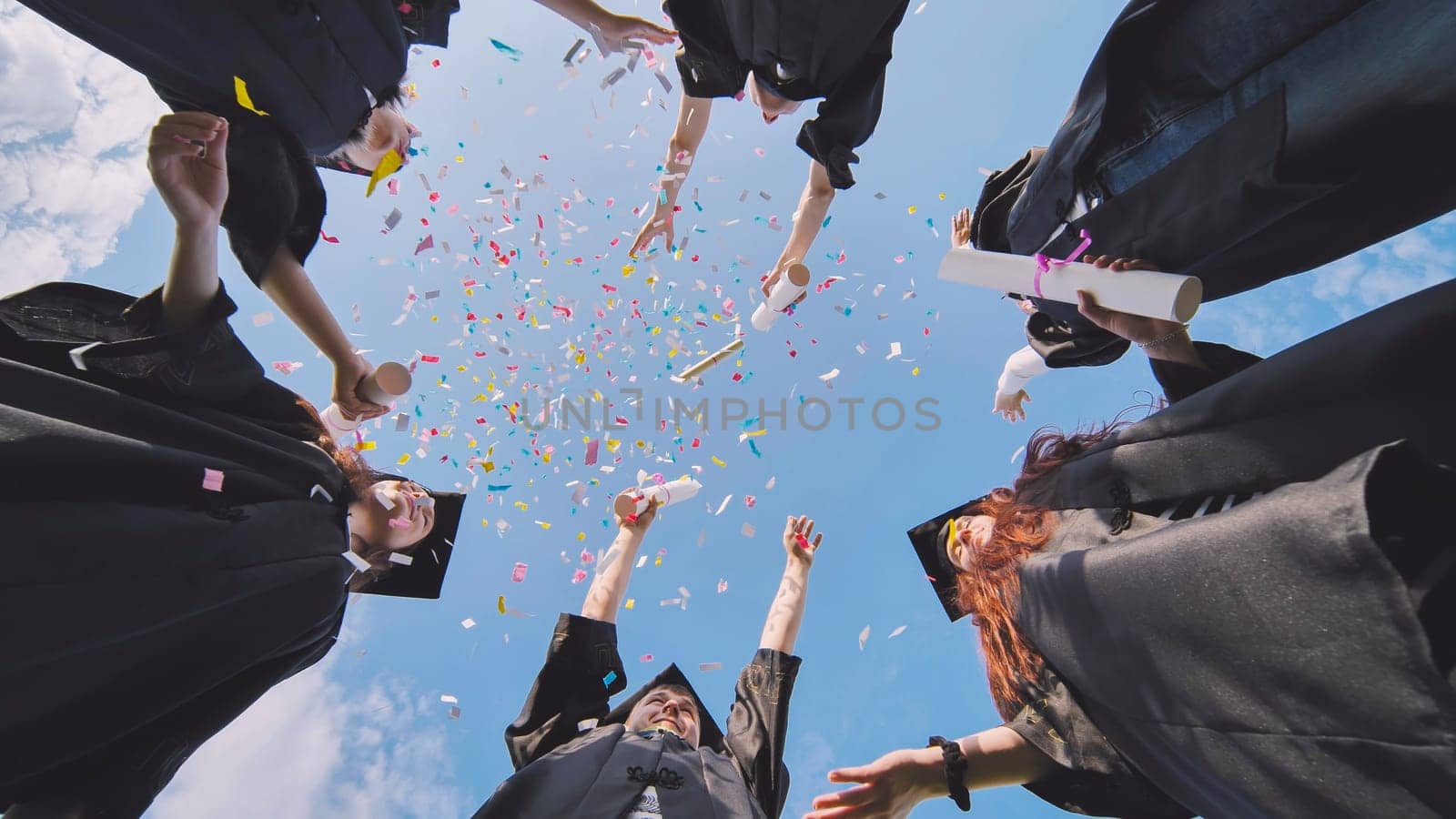 Happy graduates throwing up colorful confetti against the blue summer sky