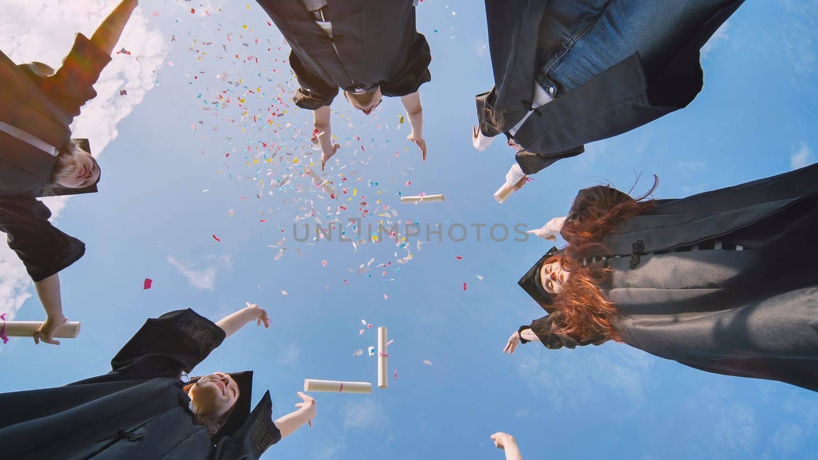 Happy graduates throwing up colorful confetti against the blue summer sky. by DovidPro