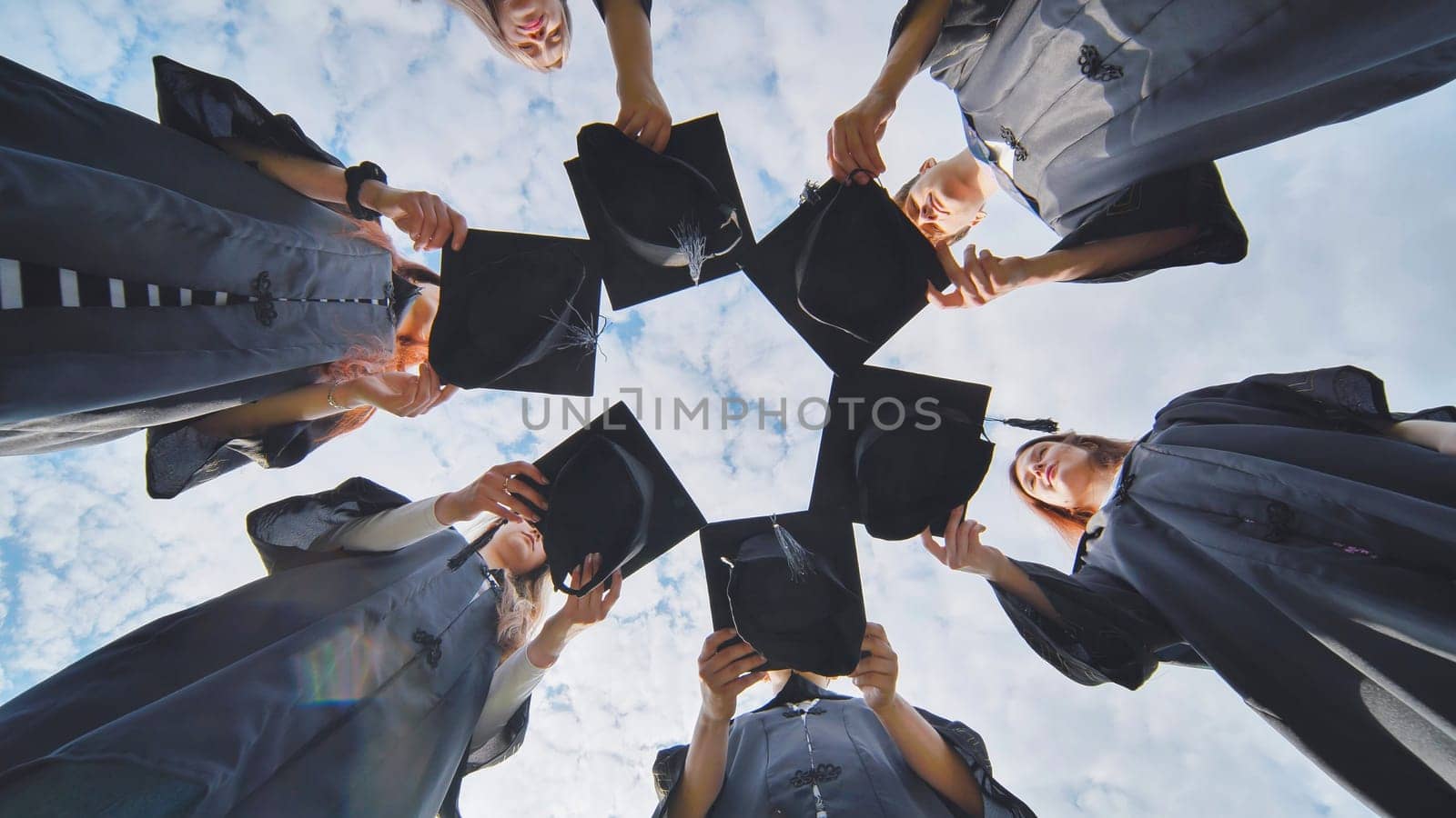 Graduates in black robes join their caps in a circle