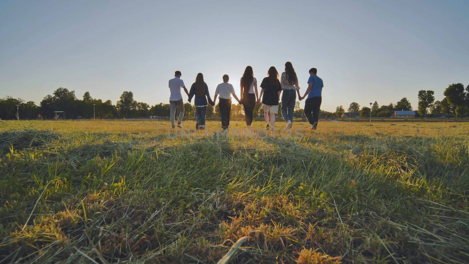 Friends at sunset holding hands walking towards the sun. by DovidPro