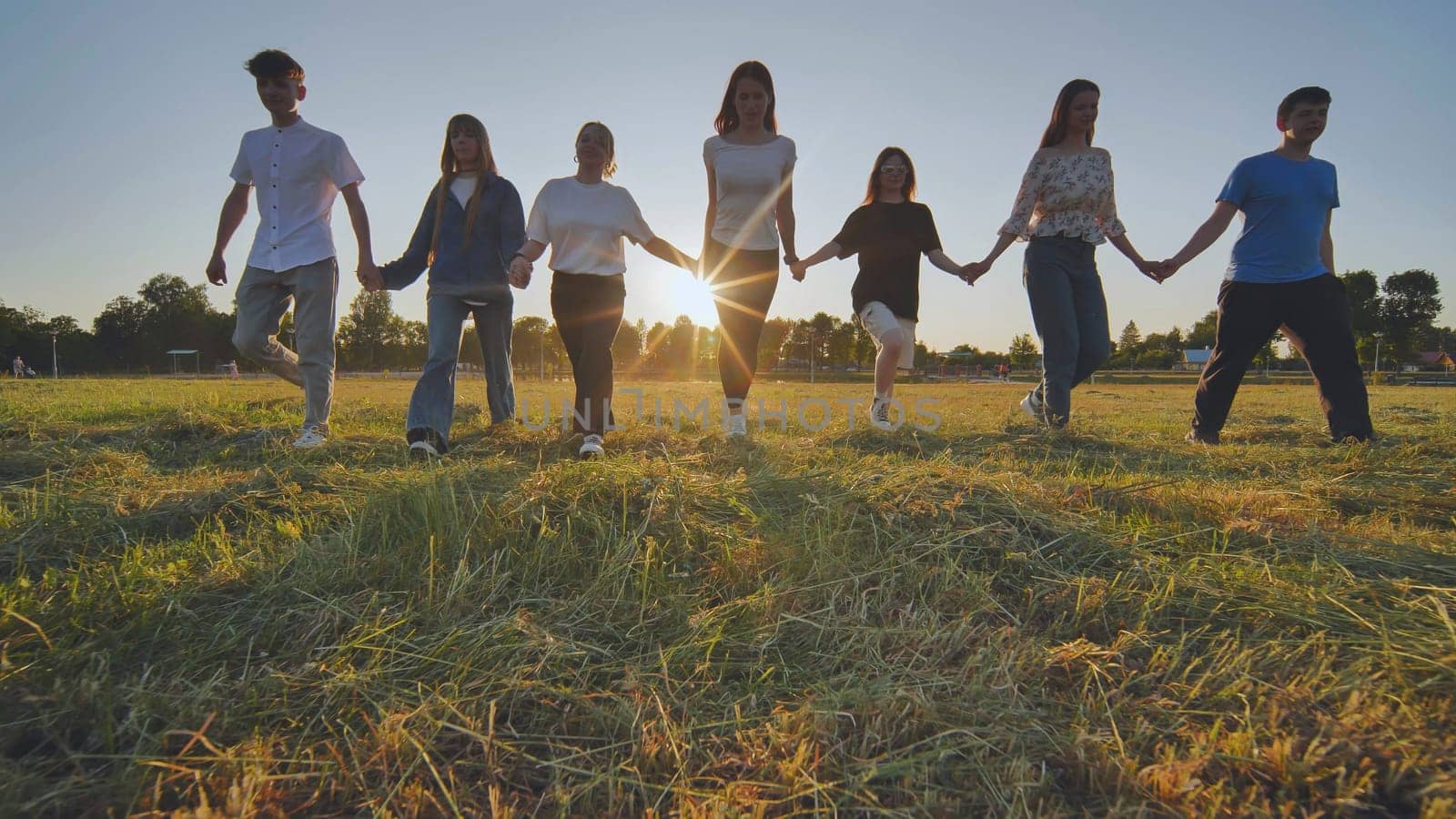 Friends at sunset holding hands walking towards the sun