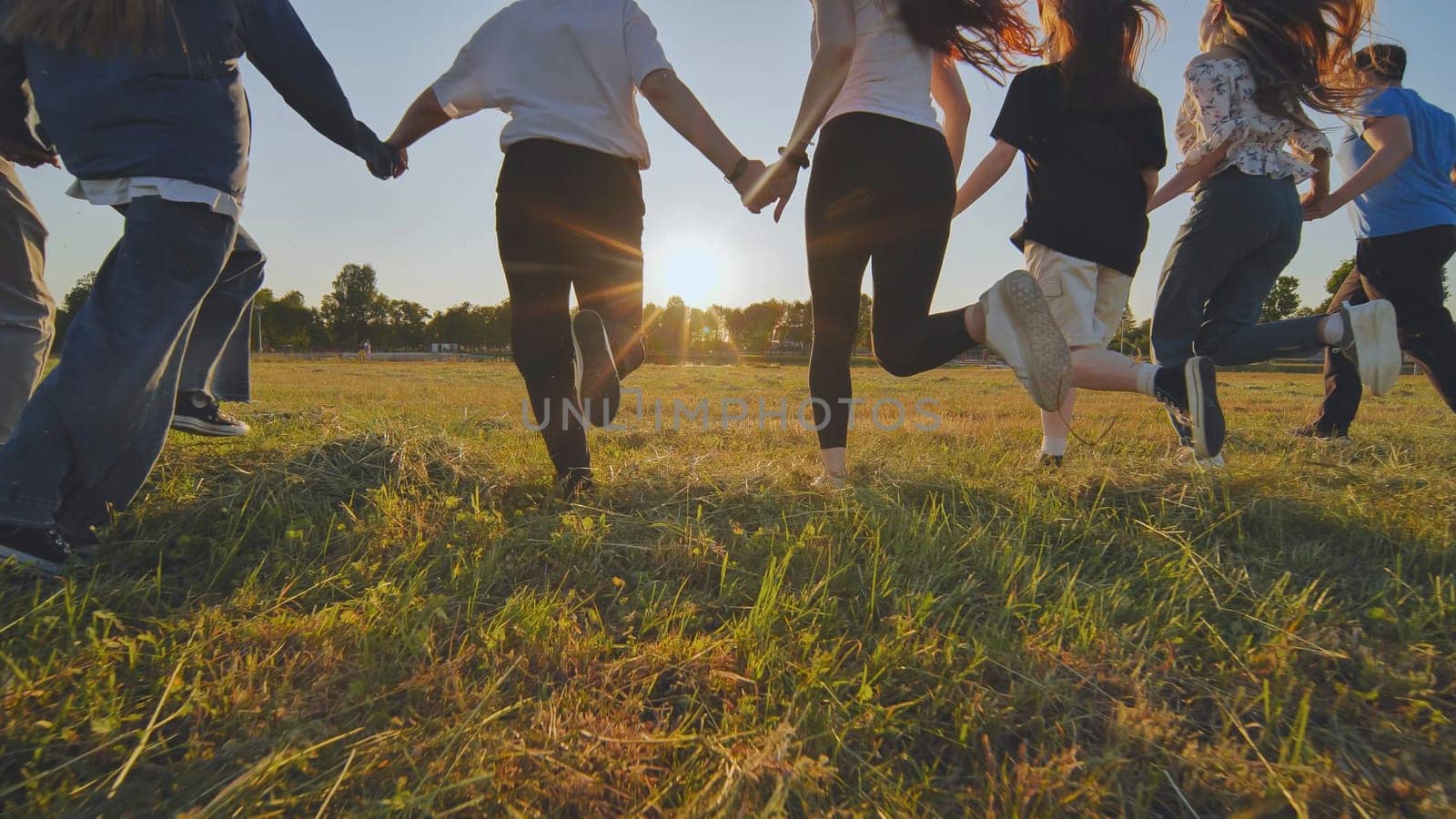 Young boys running at sunset across the field holding hands. by DovidPro