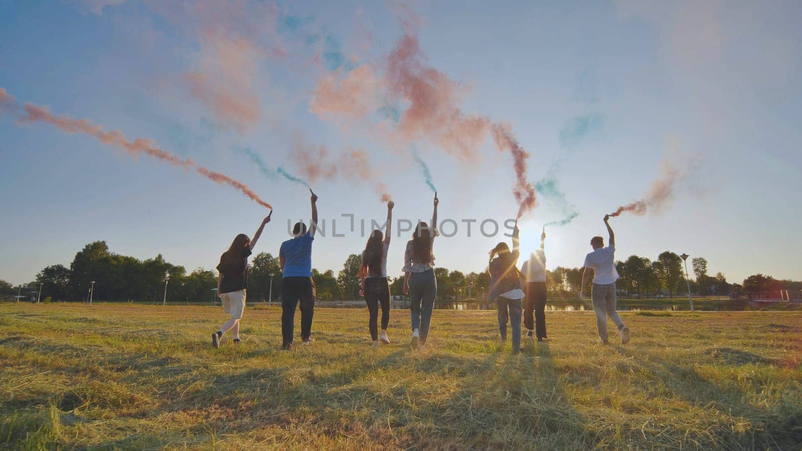 A group of friends spraying multi-colored smoke at sunset